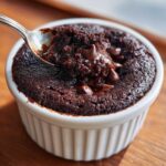 A spoonful of rich, fudgy Cottage Cheese Microwave Brownie being lifted from a white ramekin, showing melted chocolate chips.