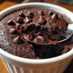 A spoonful of moist Cottage Cheese Microwave Brownie topped with melted chocolate chips being lifted from a white ramekin.