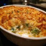 A creamy, cheesy broccoli casserole with a golden, crunchy topping served in a white oval baking dish.