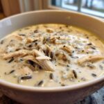 Close-up of a creamy chicken wild rice soup, featuring shredded chicken and dark wild rice grains.