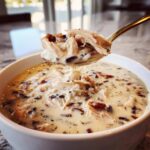 A spoonful of creamy chicken wild rice soup being lifted from a white bowl.