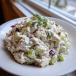 A close-up mound of creamy cottage cheese chicken salad mixed with green celery and red onion, garnished with fresh dill.