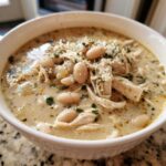 Close-up of a bowl of creamy crockpot white chicken chili topped with shredded chicken, white beans, and parsley.