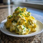 A mound of creamy egg salad recipe, rich yellow in color and topped generously with fresh green chopped chives, served on a white plate.