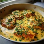 Four golden-brown chicken breasts simmering in a rich, creamy lemon sauce and topped with fresh chopped parsley.