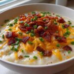 Close-up of a creamy potato soup recipe topped generously with shredded cheddar cheese, crispy bacon bits, and fresh chives.