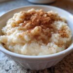 Close-up of creamy rice pudding served in a white bowl, generously dusted with cinnamon.
