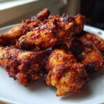 A close-up of several perfectly cooked, crispy air fryer chicken wings piled on a white plate.