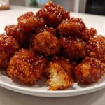 A mound of crispy, glazed orange chicken recipe pieces piled high on a white plate, showing a bite taken out.
