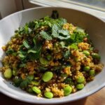 A white bowl filled with golden brown crispy rice salad mixed with bright green edamame and topped generously with fresh mint and cilantro.