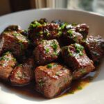 Close-up of tender crockpot steak bites coated in sauce and sprinkled with fresh green herbs.