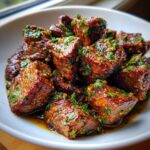 Close-up of tender, glazed crockpot steak bites topped with fresh parsley and garlic.