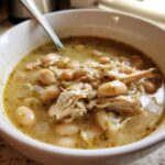 Close-up of a white bowl filled with hearty crockpot white chicken chili, showing shredded chicken and white beans in a savory broth.