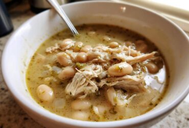 Close-up of a white bowl filled with hearty crockpot white chicken chili, showing shredded chicken and white beans in a savory broth.