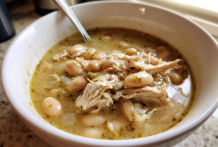 Close-up of a white bowl filled with hearty crockpot white chicken chili, showing shredded chicken and white beans in a savory broth.