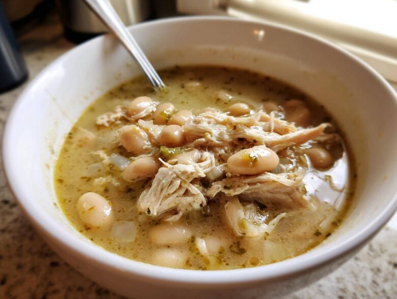 Close-up of a white bowl filled with hearty crockpot white chicken chili, showing shredded chicken and white beans in a savory broth.