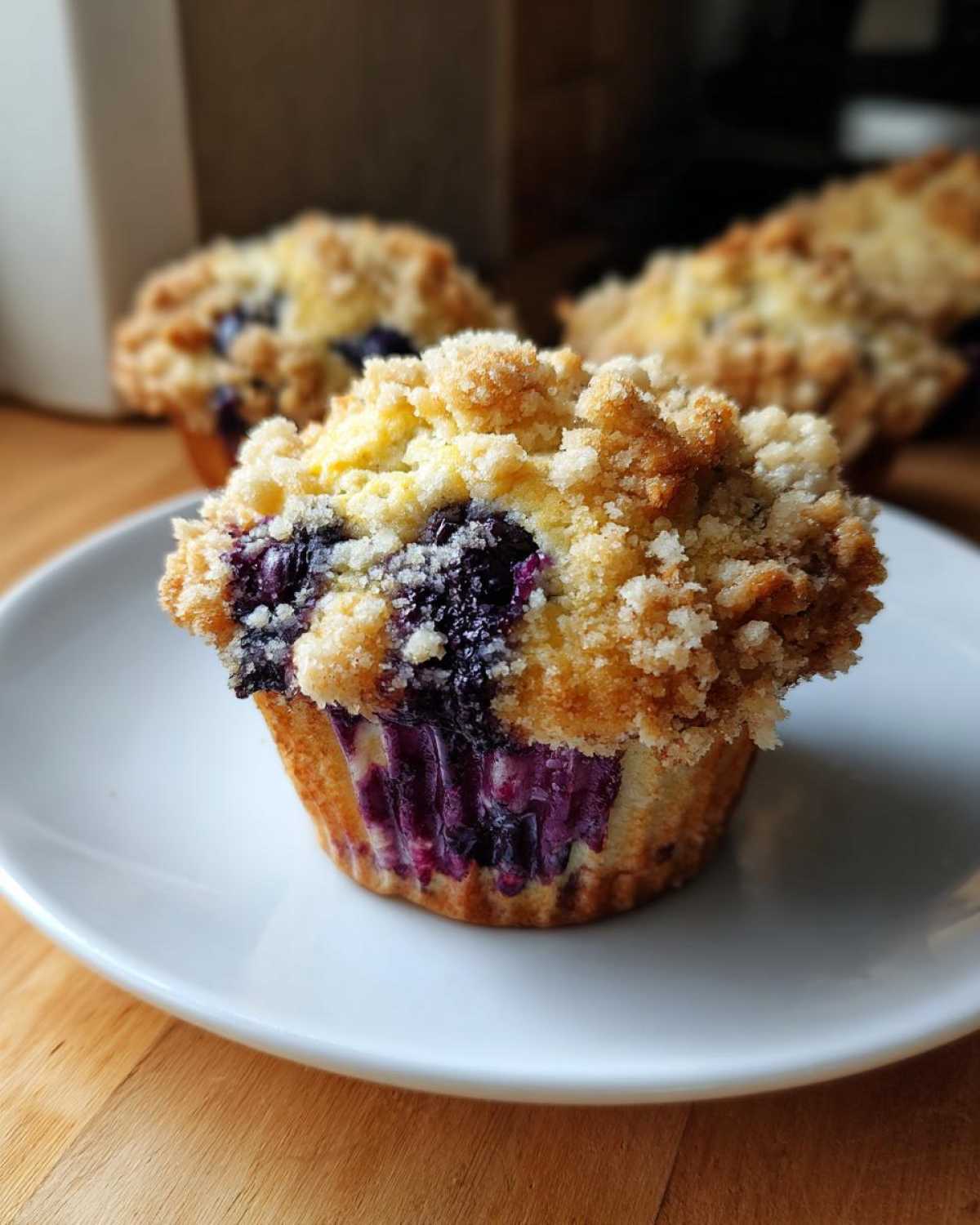 A close-up of a fresh blueberry muffin topped with golden streusel served on a white plate.
