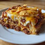 A close-up serving of Ultimate Dorito Casserole layered with meat, sauce, melted cheese, and topped with chips.