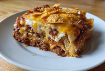 A close-up serving of Ultimate Dorito Casserole layered with meat, sauce, melted cheese, and topped with chips.