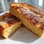 Two thick slices of golden brown easy french toast dusted with powdered sugar on a white plate.