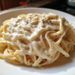 Close-up of fettuccine pasta coated in rich homemade alfredo sauce and topped with black pepper.