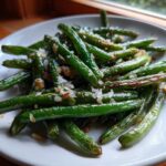 Close-up of bright green beans seasoned with coarse salt and browned bits, served on a white plate.