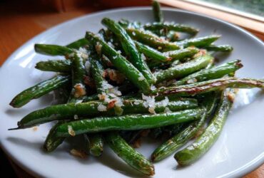 Close-up of bright green beans seasoned with coarse salt and browned bits, served on a white plate.