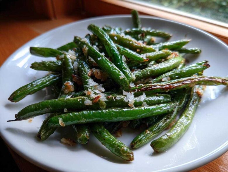 Close-up of bright green beans seasoned with coarse salt and browned bits, served on a white plate.