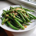 Bright green beans tossed with toasted, seasoned breadcrumbs served on a white plate.