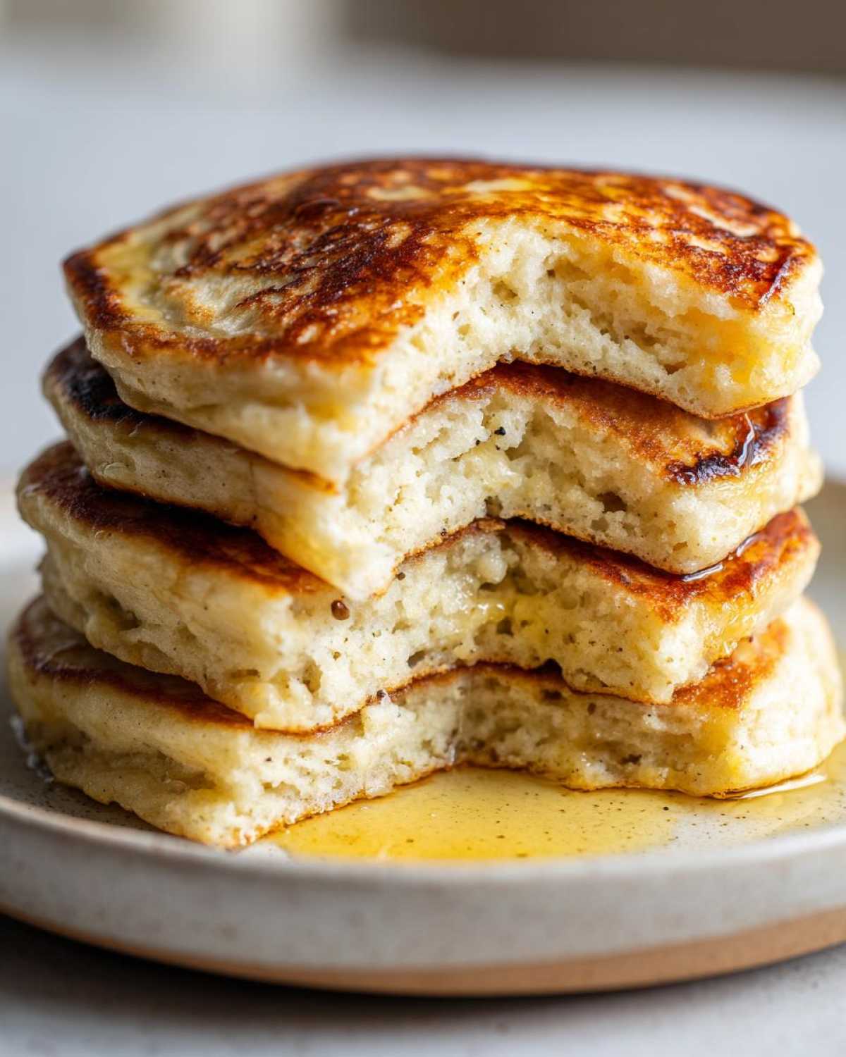 Close-up of a stack of four fluffy almond flour pancakes with a bite taken out, drizzled with syrup.