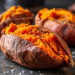 Close-up of a fluffy baked sweet potato, split open and seasoned with salt and pepper.