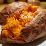 Close-up of a fluffy baked sweet potatoes split open and topped with coarse sea salt.