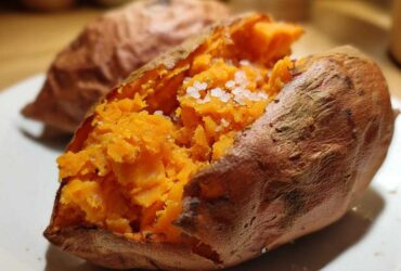 Close-up of a fluffy baked sweet potatoes split open and topped with coarse sea salt.
