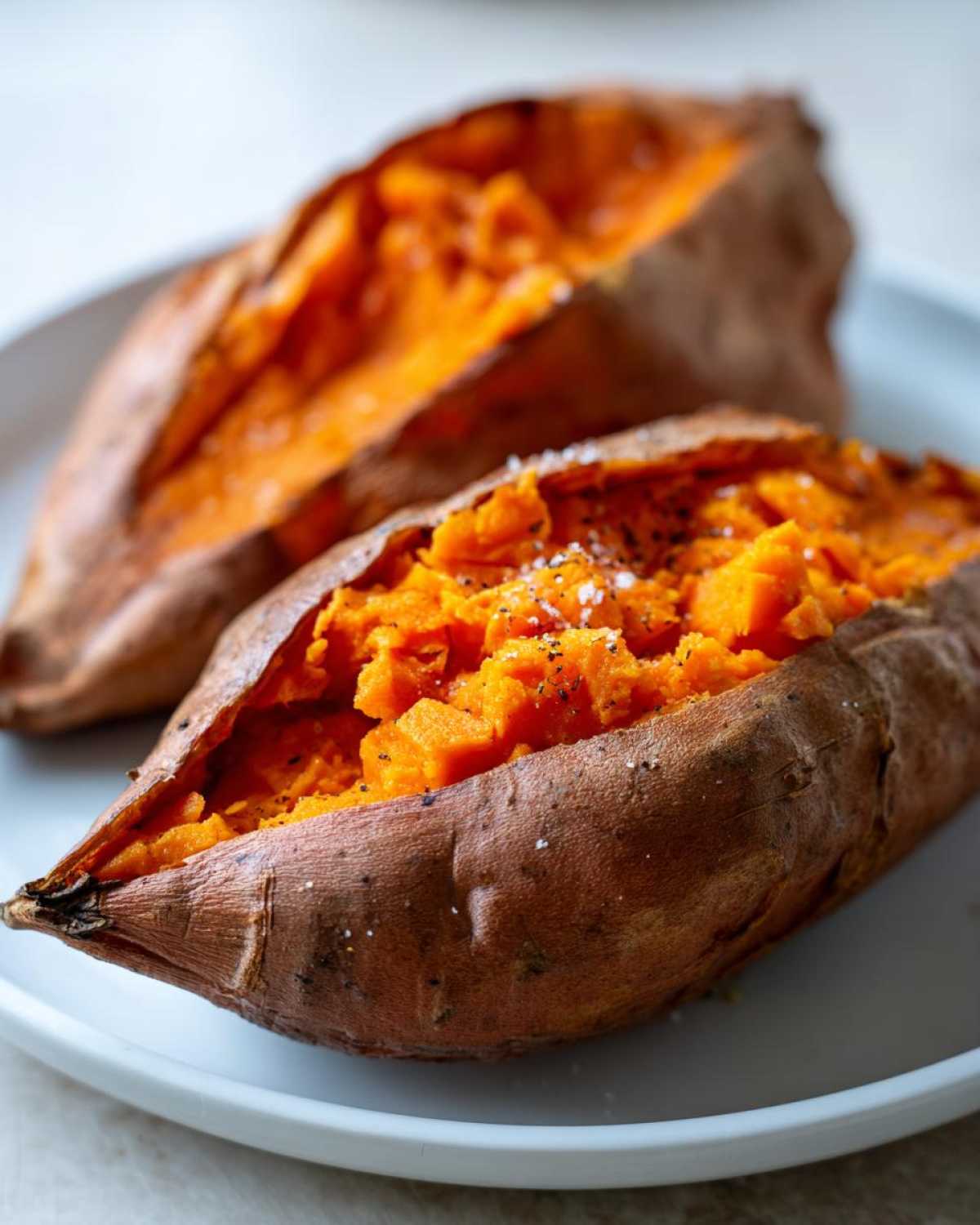 Two fluffy baked sweet potatoes, split open and seasoned with salt and pepper, ready to eat.