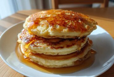 A tall stack of three fluffy banana pancakes drizzled generously with golden syrup.