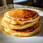Close-up of a stack of three fluffy greek yogurt pancakes with golden brown tops.
