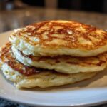 A close-up stack of three fluffy greek yogurt pancakes with golden brown tops served on a white plate.