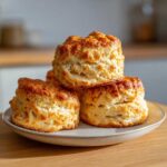 A stack of three golden-brown, tall, and fluffy scones resting on a small ceramic plate.