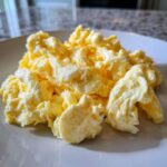 Close-up of incredibly fluffy scrambled eggs with soft curds served on a white plate.