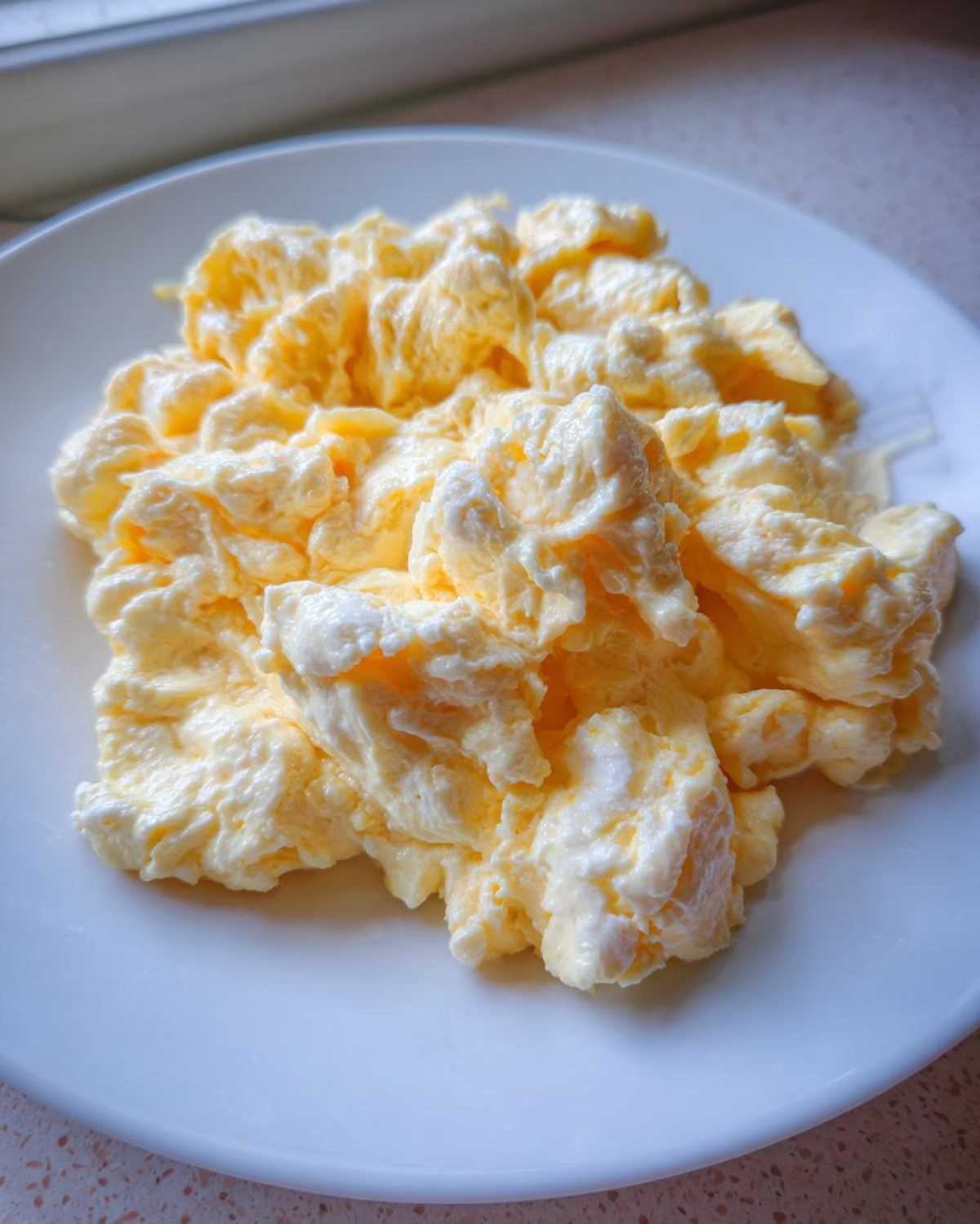 A close-up of incredibly fluffy scrambled eggs piled high on a white plate, showing soft curds.