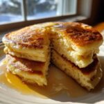 Close-up of a stack of fluffy sourdough pancakes, cut open to show the texture, drizzled with melted butter and syrup.