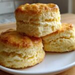 A stack of three tall, fluffy, golden brown scones displayed on a white plate.