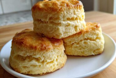 A stack of three tall, fluffy, golden brown scones displayed on a white plate.