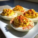 Four perfectly piped deviled eggs sprinkled generously with bright red paprika, resting on a white plate.