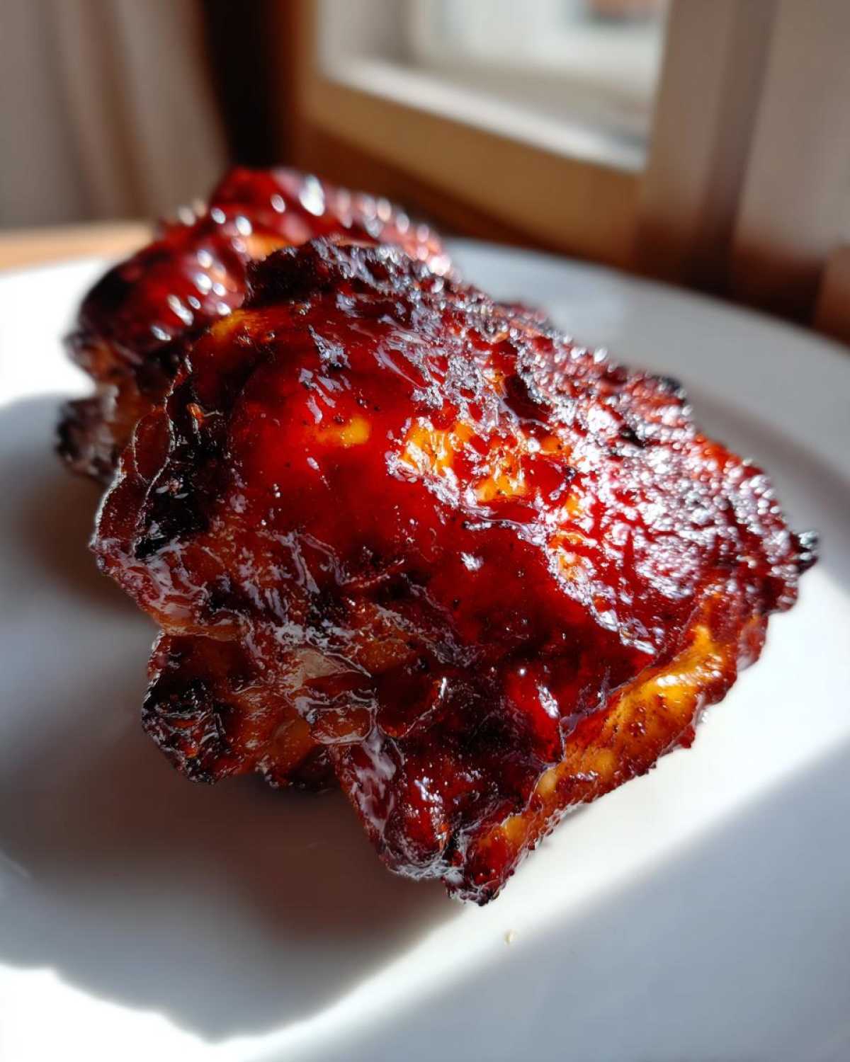 Close-up of two pieces of juicy bbq chicken covered in a thick, glossy, dark red barbecue sauce.