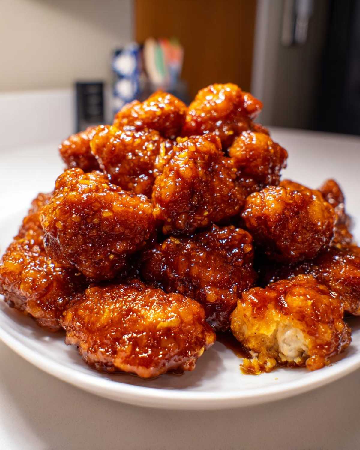 Close-up of a mound of crispy, glazed pieces from an orange chicken recipe piled high on a white plate.