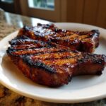 Two beautifully caramelized and grilled pork steak recipe cuts resting on a white plate.