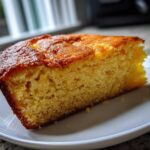 A close-up of a thick, golden slice of moist skillet cornbread served on a white plate.