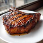 Close-up of a thick, grilled bone-in pork chop coated in a sticky, dark marinade for pork chops.