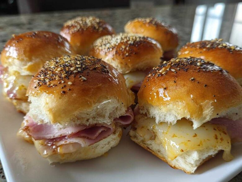 A plate of warm Ham and Cheese Sliders featuring melted cheese and poppy seed topping.